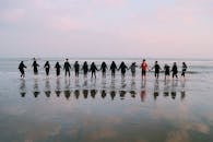 pexels photo 1756665 1756665 A large group holding hands at the beach during sunset, reflecting in the water.