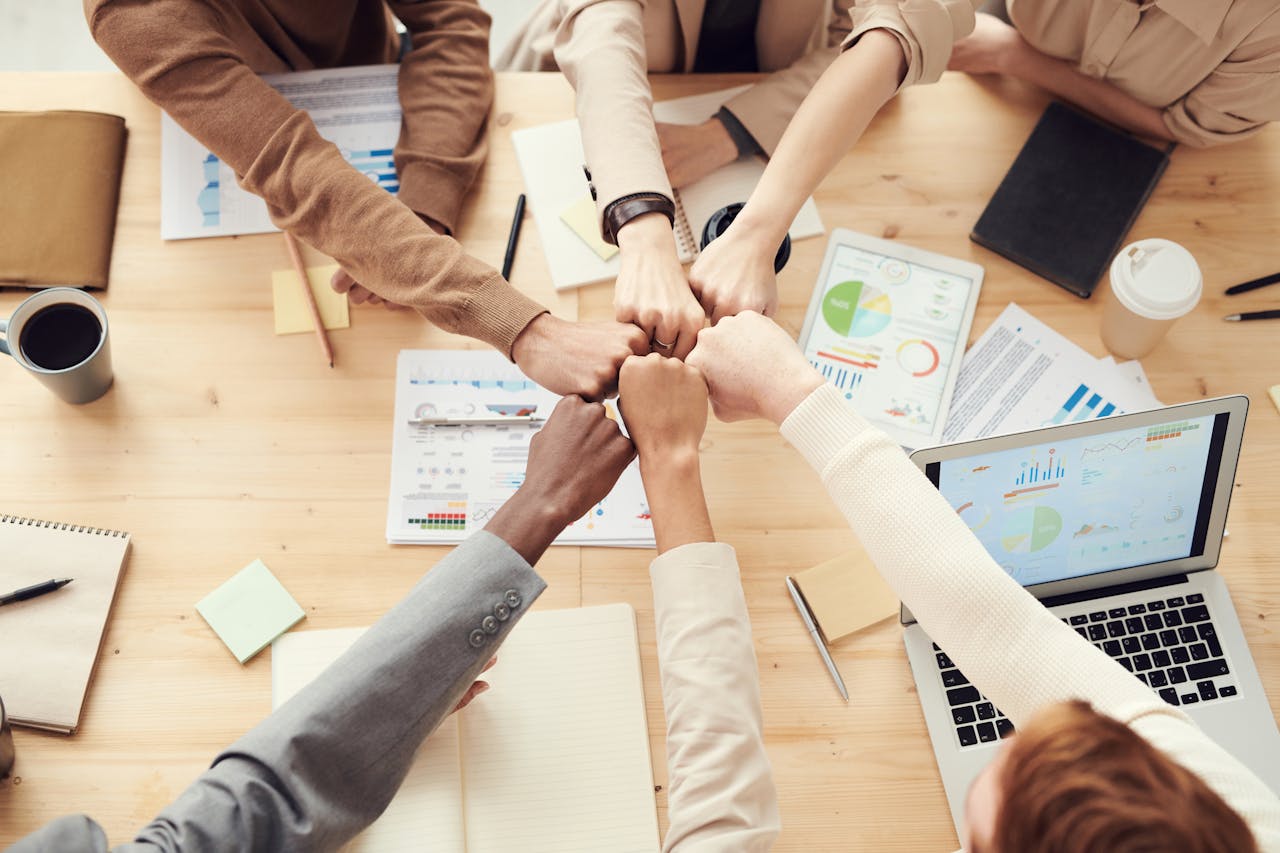 creative-02 Top view of a diverse team fist bumping over a meeting table with paperwork and laptops, symbolizing teamwork.